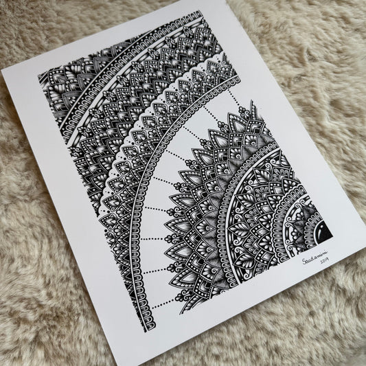 Hand-drawn mandala fragment by Saudamini Madra in black ink on Bristol paper, showing concentric arcs of fine patterning, photographed on textured surface