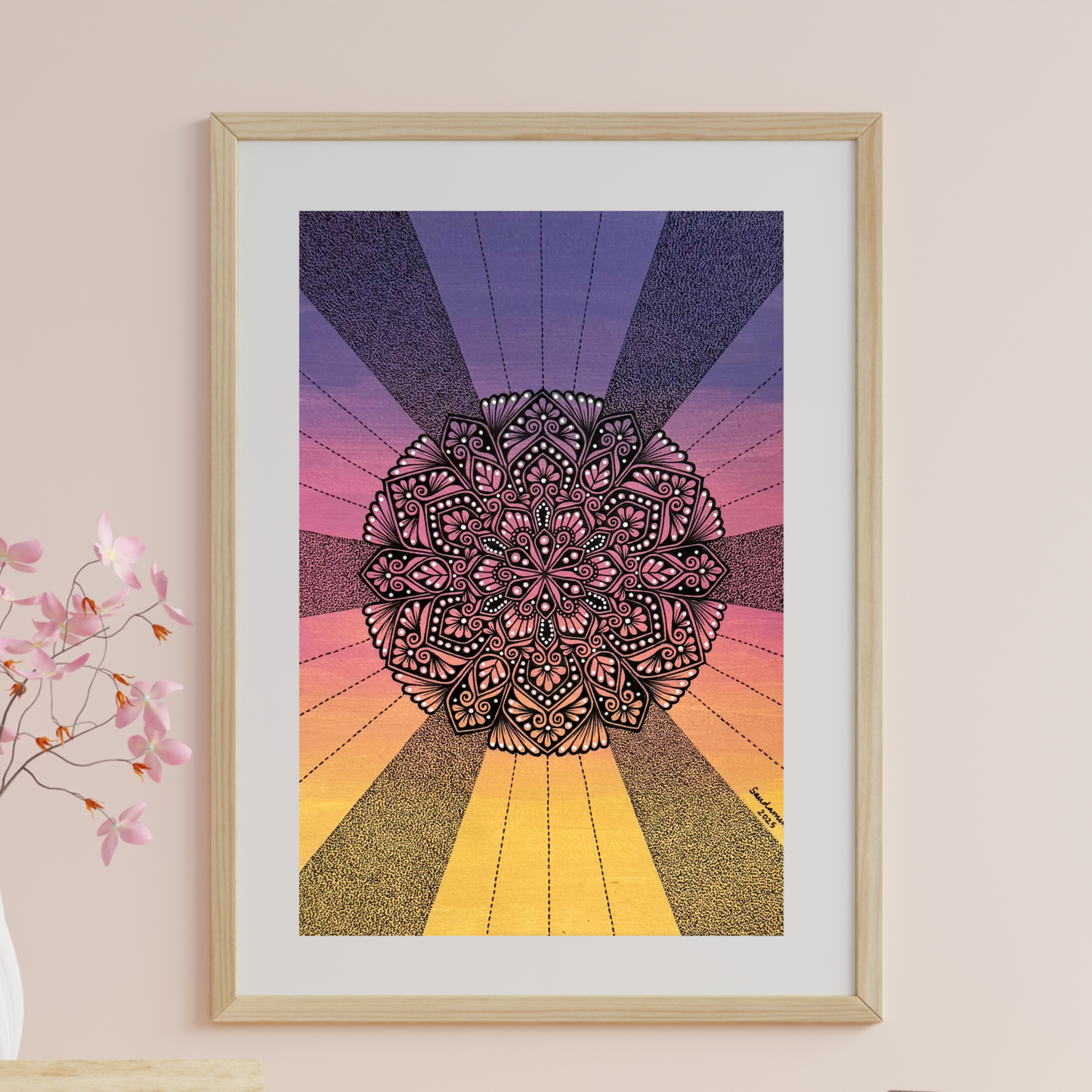 Framed mandala art with a colorful radial design on a pink wall.