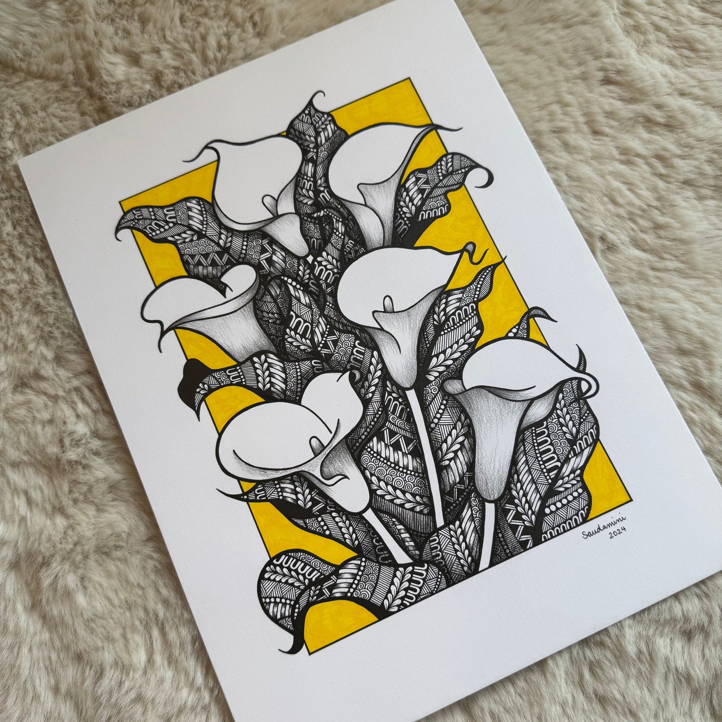 Hand-drawn calla lilies zentangle by Saudamini Madra in black ink on Bristol paper with amber background, photographed on textured surface