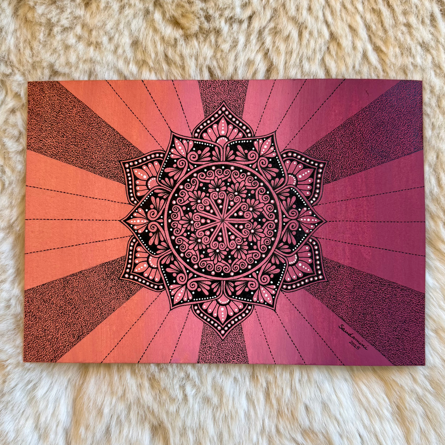 Mandala design on a card with a pink and orange gradient background, placed on a fluffy white surface.