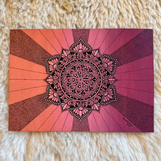 Mandala design on a card with a pink and orange gradient background, placed on a fluffy white surface.