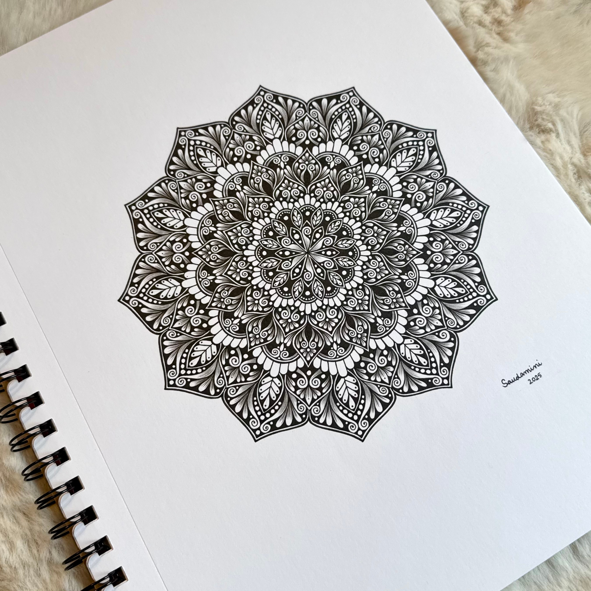 Black mandala drawing on a white sheet of paper with a spiral binding.