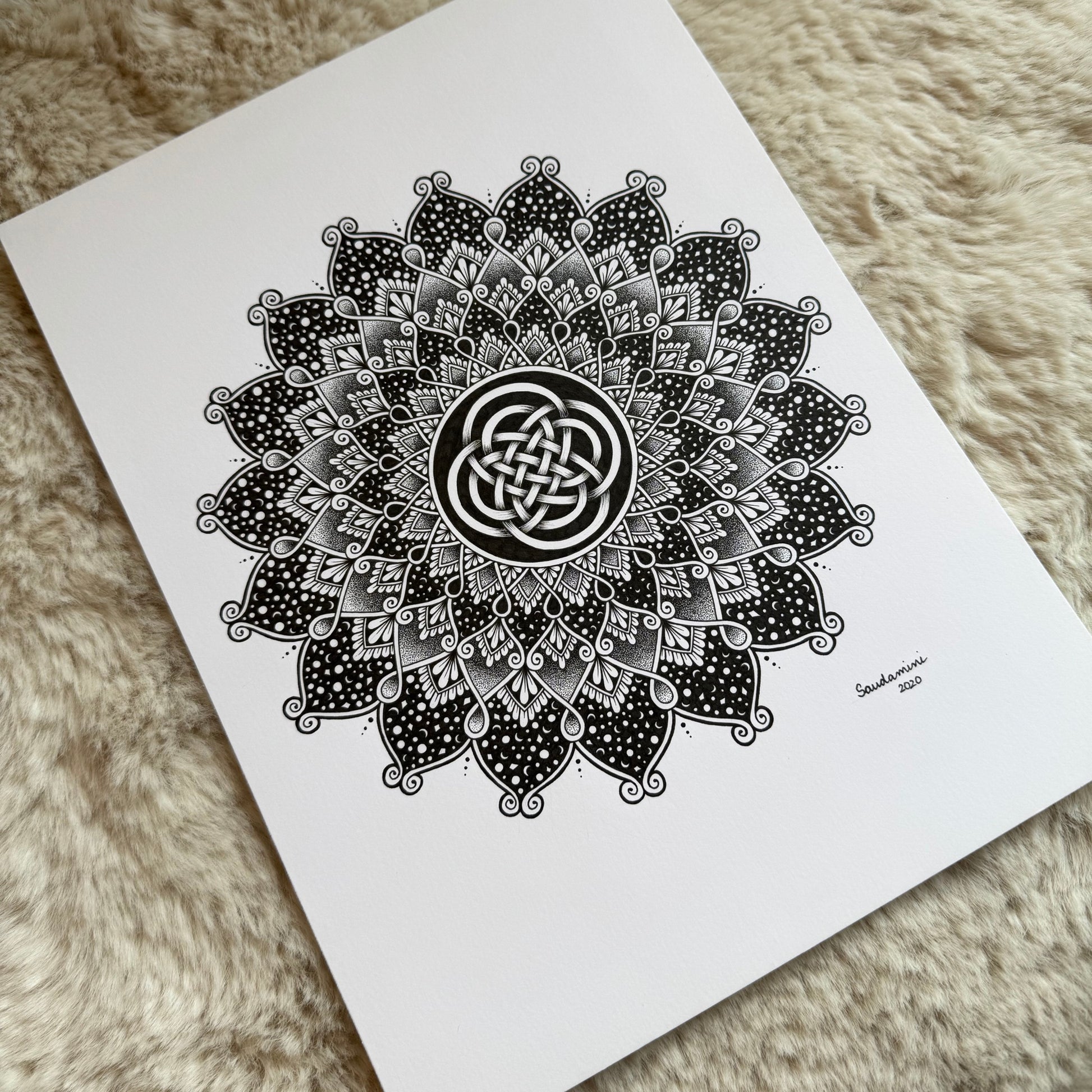 Hand-drawn mandala by Saudamini Madra with interlaced knot center in black ink on Bristol paper, photographed on textured surface