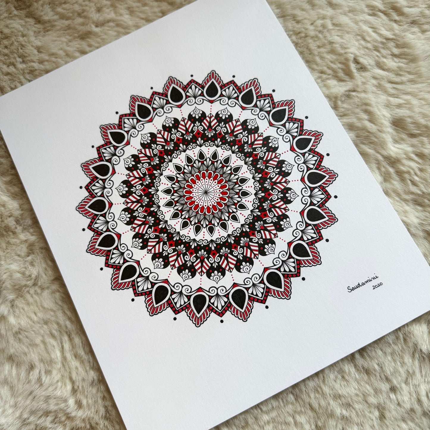 Hand-drawn mandala by Saudamini Madra in black and red ink on Bristol paper, photographed on textured surface