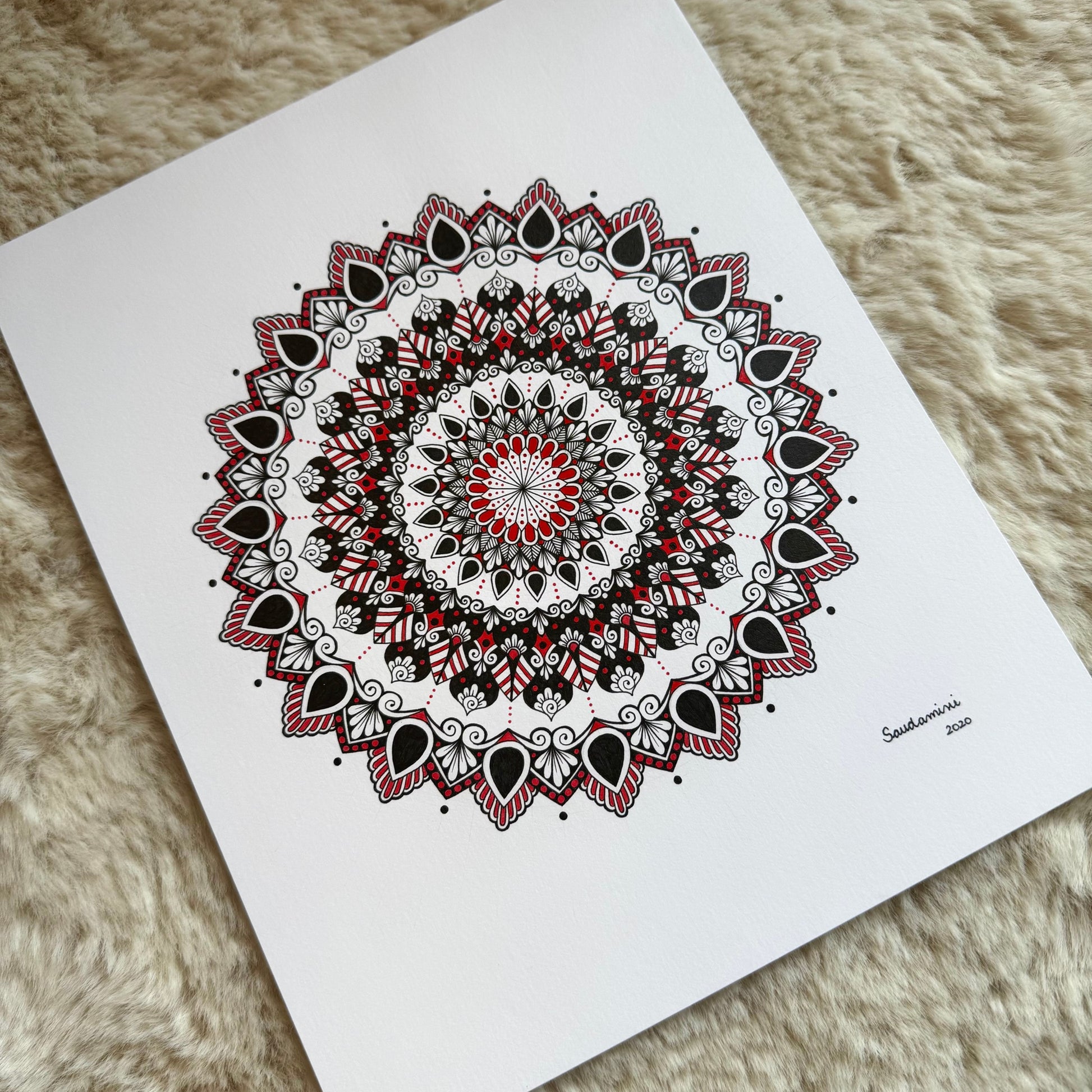 Hand-drawn mandala by Saudamini Madra in black and red ink on Bristol paper, photographed on textured surface