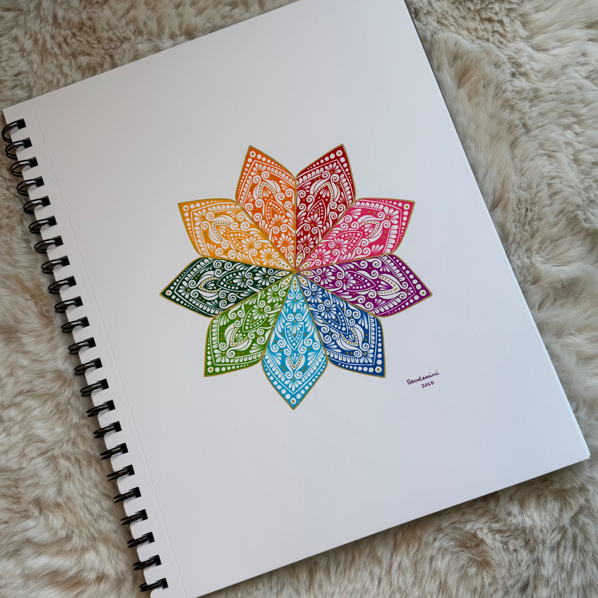 Colorful mandala drawing on a spiral-bound notebook with a fluffy beige background