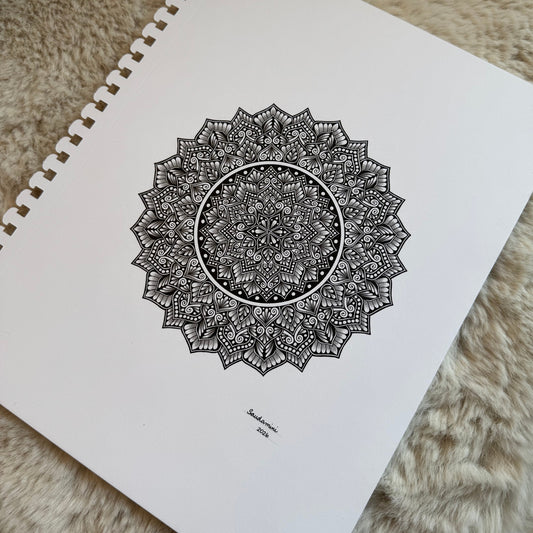 Hand-drawn mandala by Saudamini Madra in black ink on Bristol paper with open center and dense outer rings, photographed on textured surface